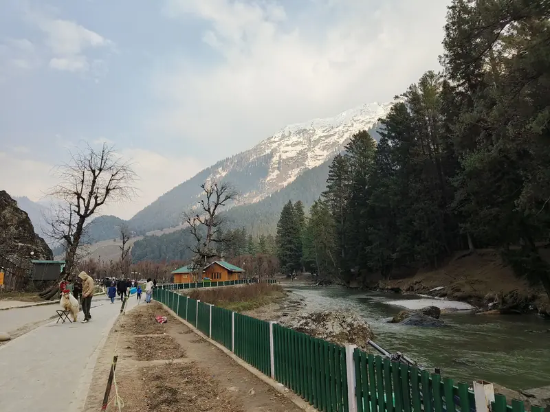 River and walking path through Betaab Valley in spring, with a snowy peak behind