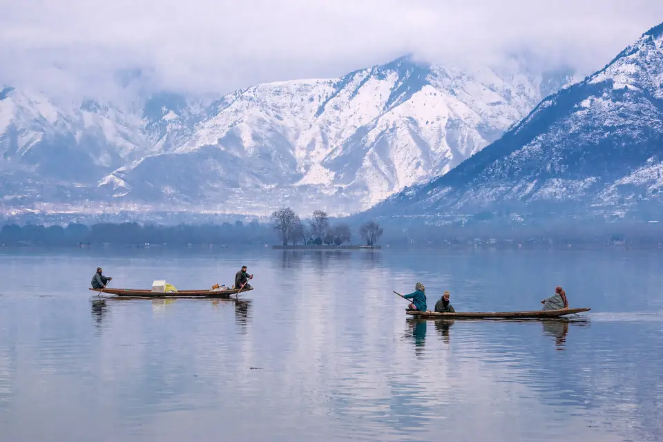 Shikaras moored on Dal Lake below snow-covered mountains in January