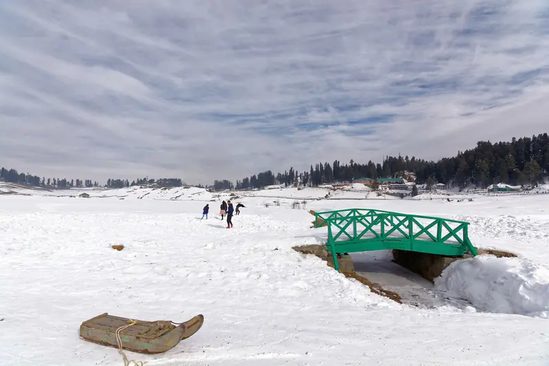 A green footbridge across the snow-covered Gulmarg meadow